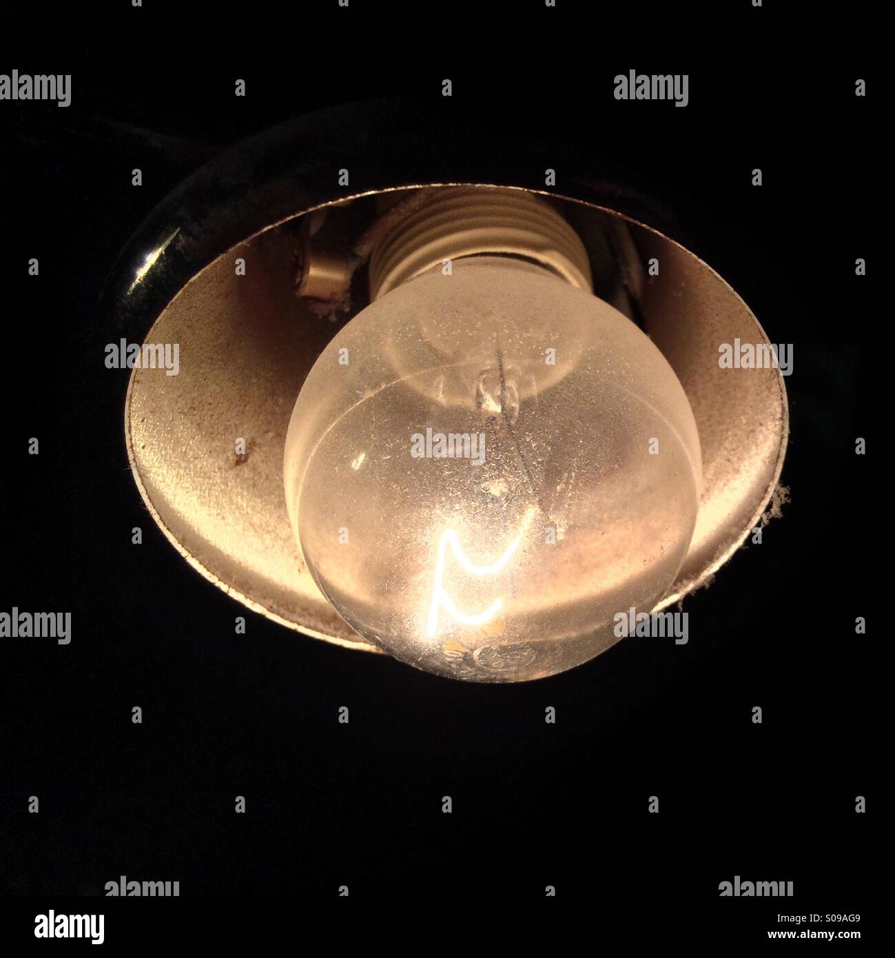 Dusty filament light bulb with metal shade on dark background Stock