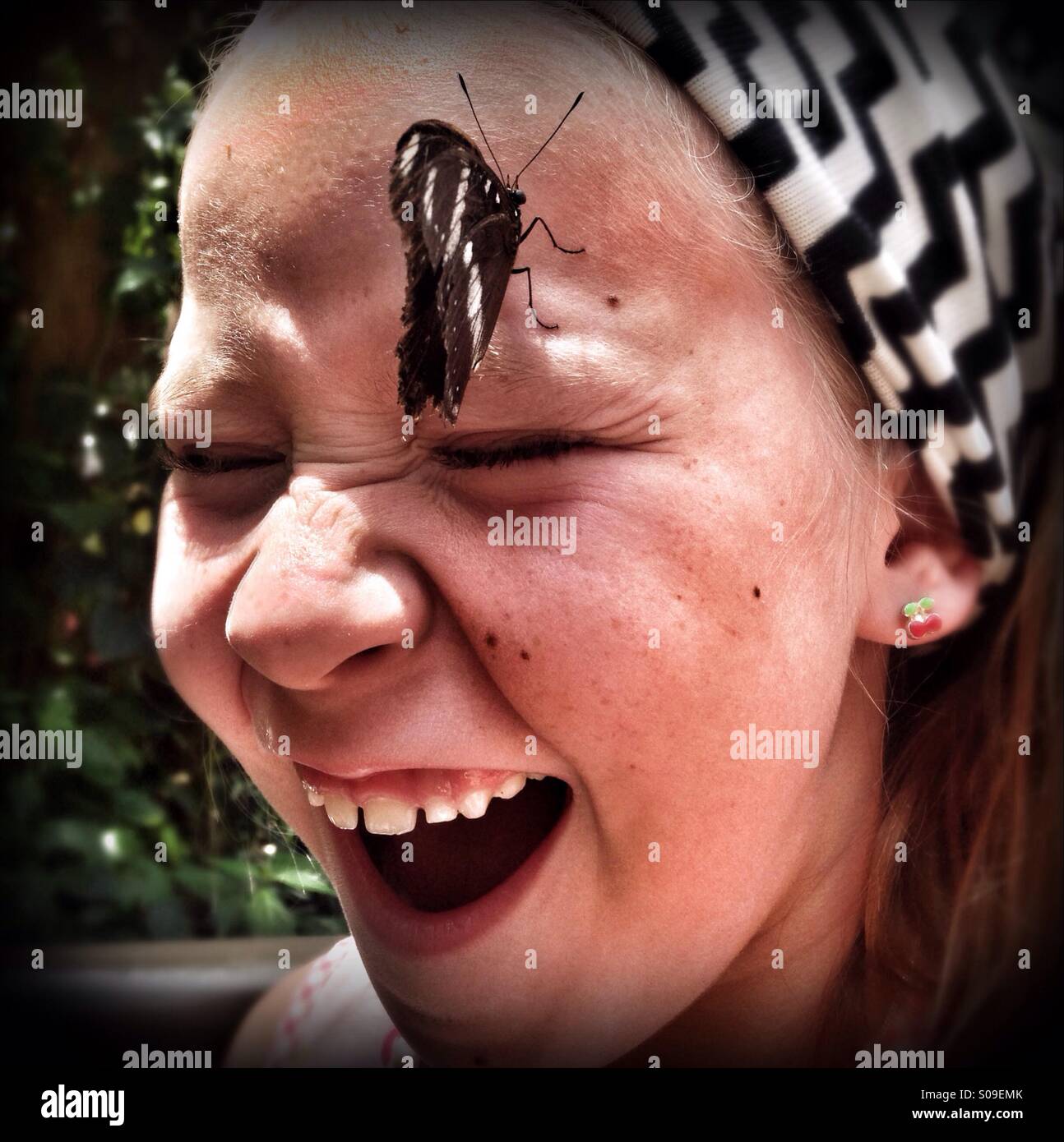 Seven years old girl reacting to a butterfly landing on her face. - Smartphone Captured Stock Image