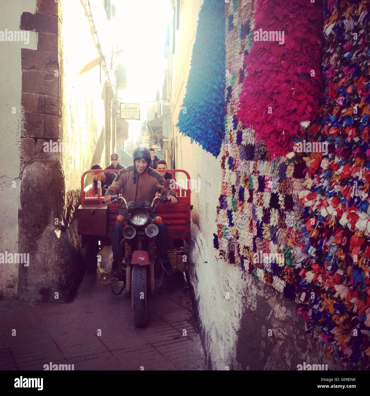 Man on motorbike squeezes through narrow lane opening, in Essaouira medina, Morocco. Stock Photo