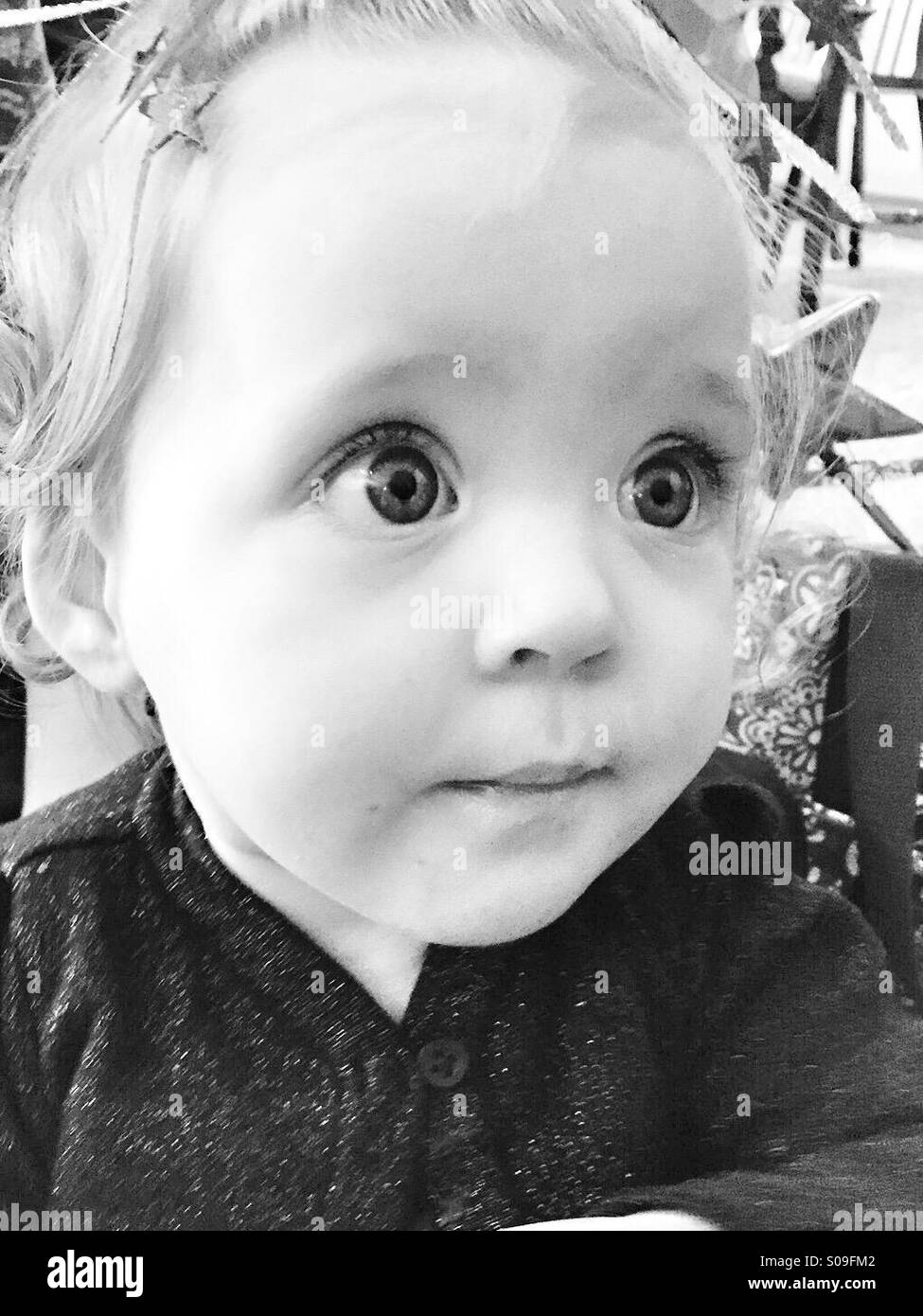 An 11 month old wide-eyed baby girl portrait in black and white. Stock Photo