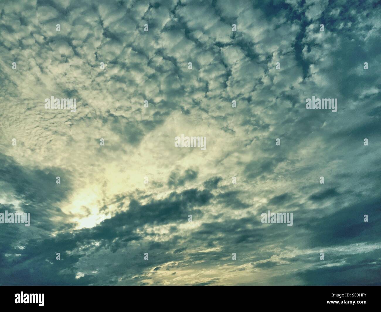 White puffy clouds across the blue sky, with the sun shining through the clouds Stock Photo