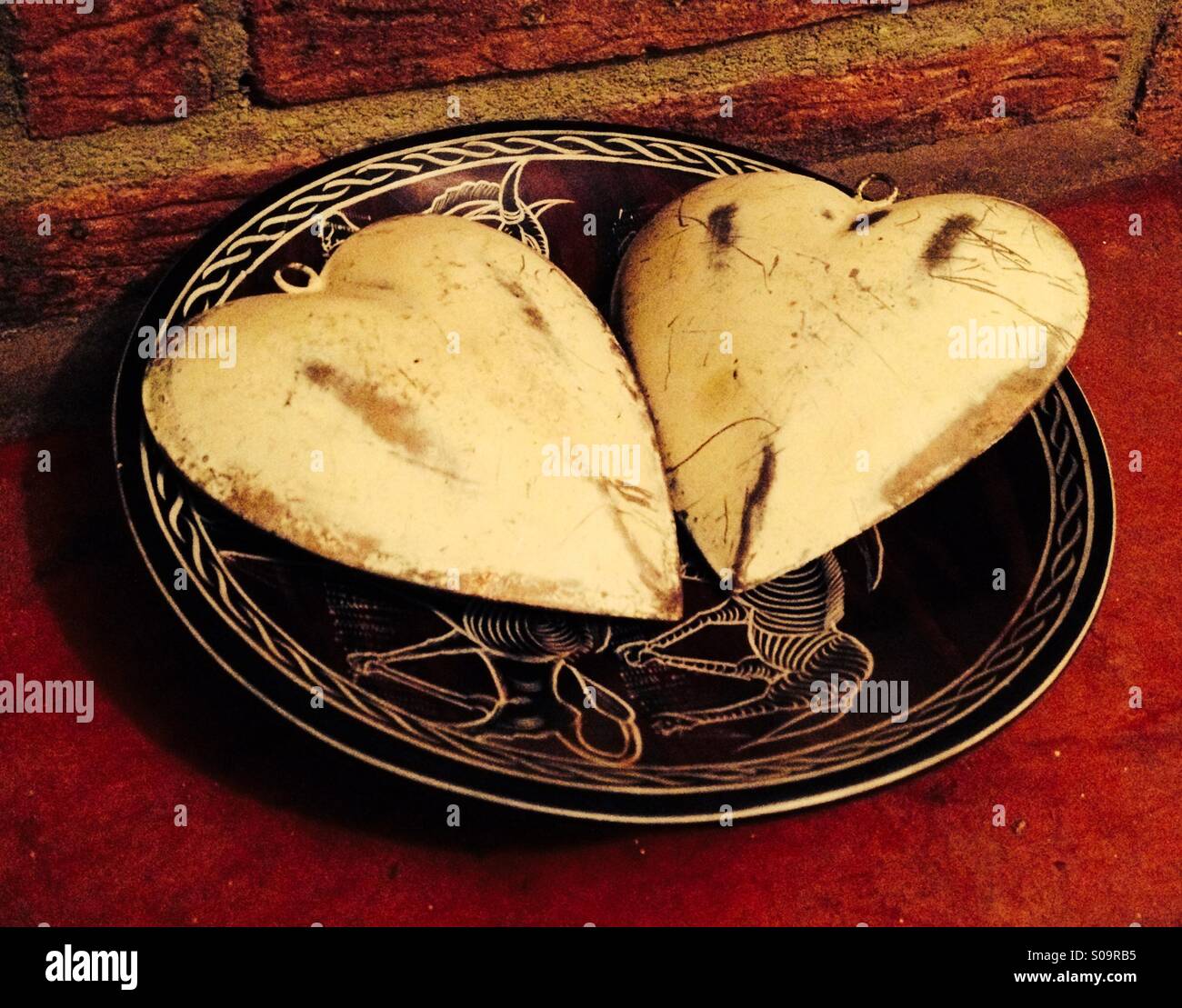 Two scratched cream hearts in a decorative bowl against a brick wall Stock Photo
