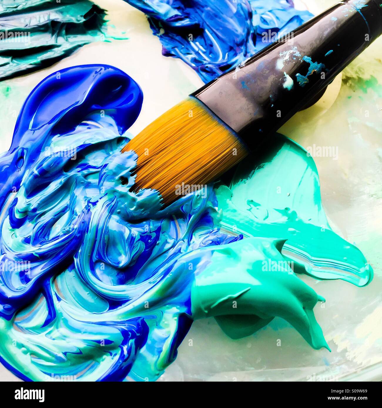 Paintbrush in blue and turquoise paint. Stock Photo