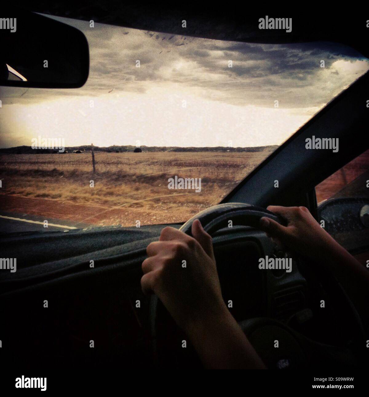 Two hands on a car steering wheel driving along a Western Australian