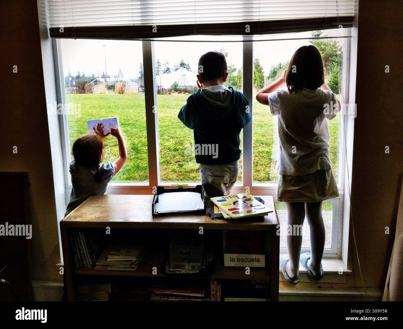 Children tracing drawings on the window glass overlooking green field ...