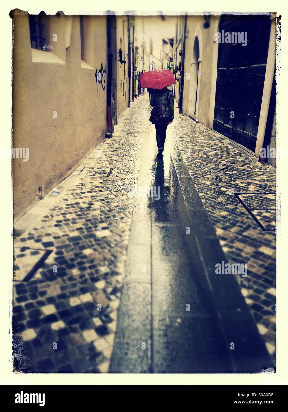 A girl seen from the back walking under the rain with a red umbrella - Smartphone Captured Stock Image