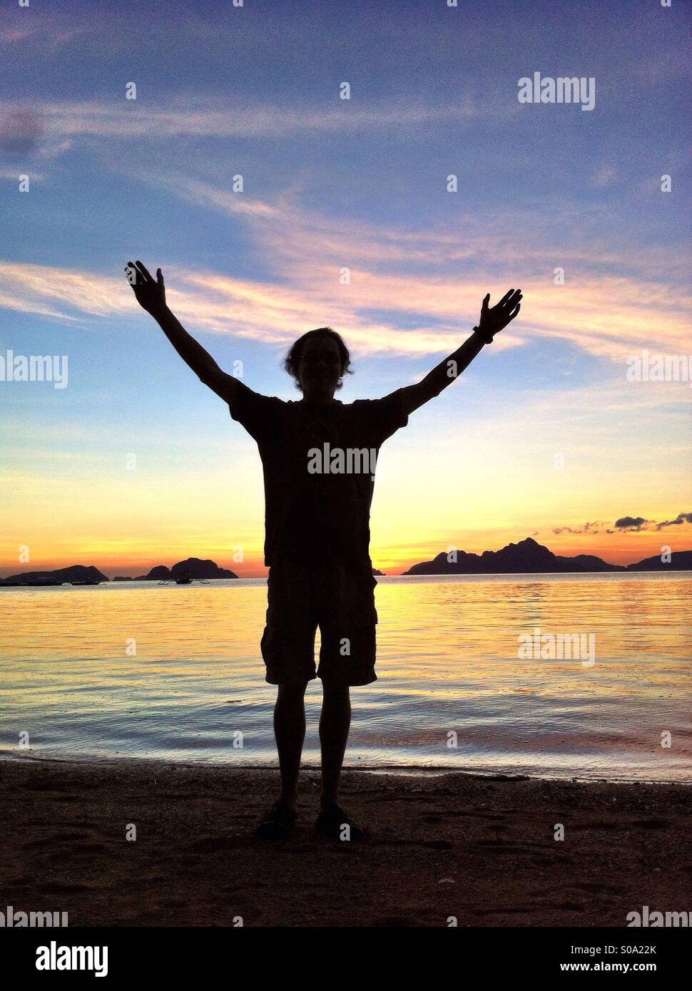 Hello world! silhouette of a man in shorts with hands up against golden sunset in El Nido on Palawan Island, Philippines. - Smartphone Captured Stock Image