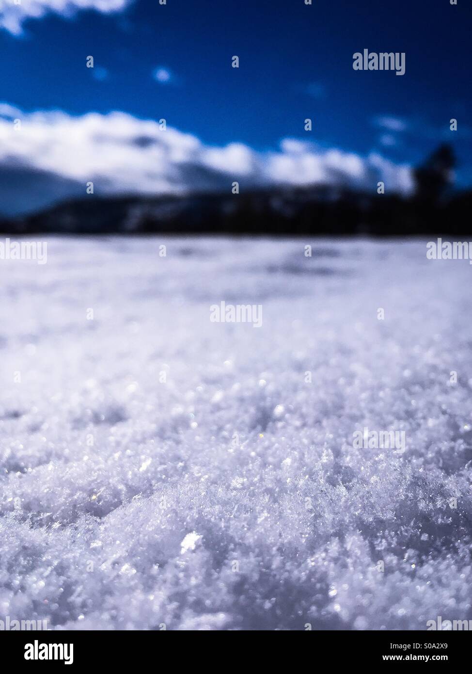 Closeup of snow crystals with out of focus blue sky background. - Smartphone Captured Stock Image