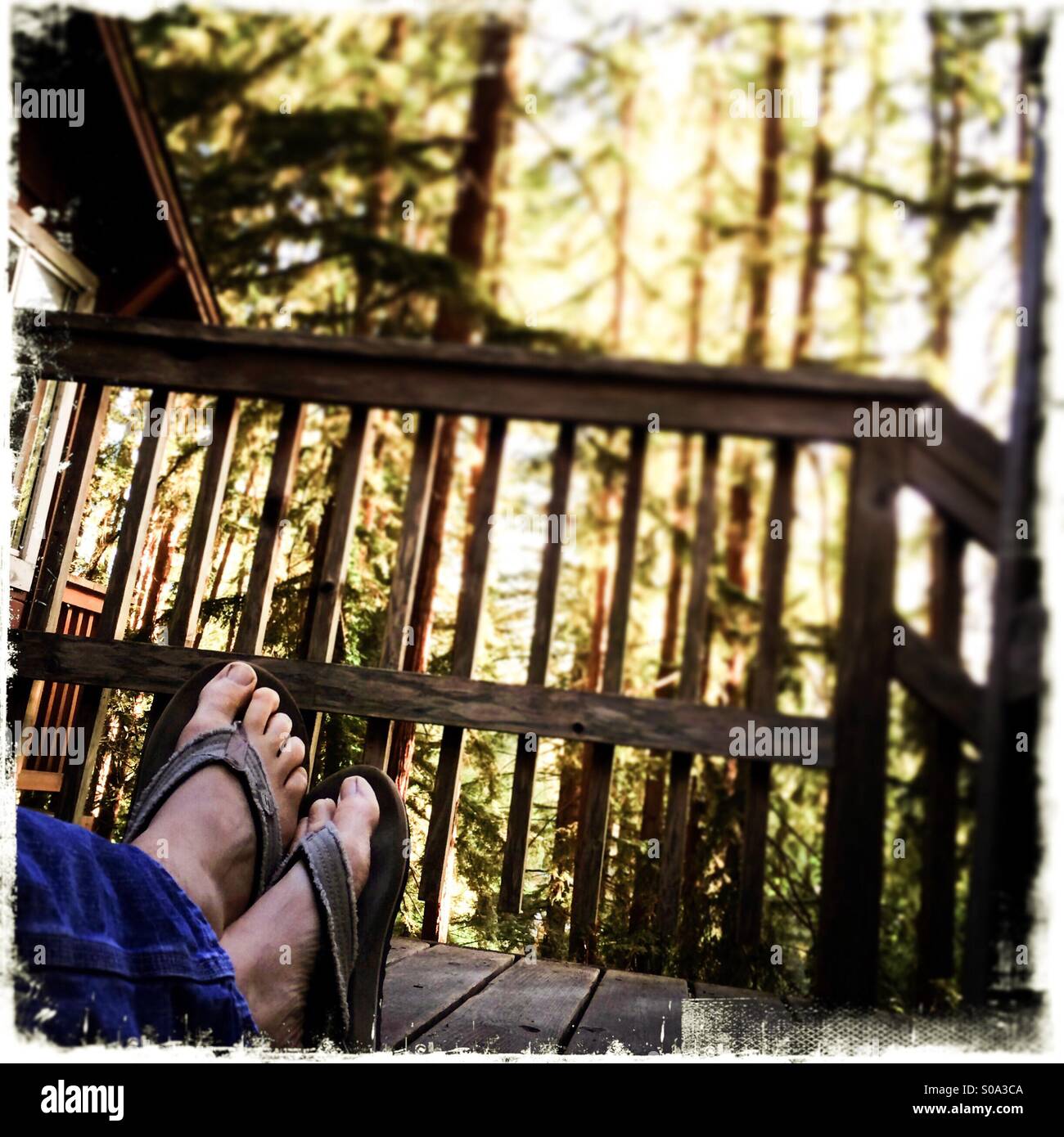A man's feet crossed while sitting on a deck in a forest. Stock Photo