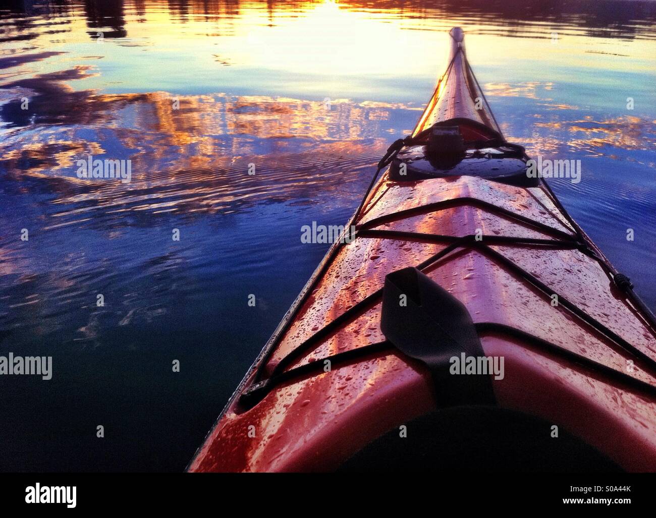 Sunset reflects in the sea water and the bow of red sea kayak - Smartphone Captured Stock Image
