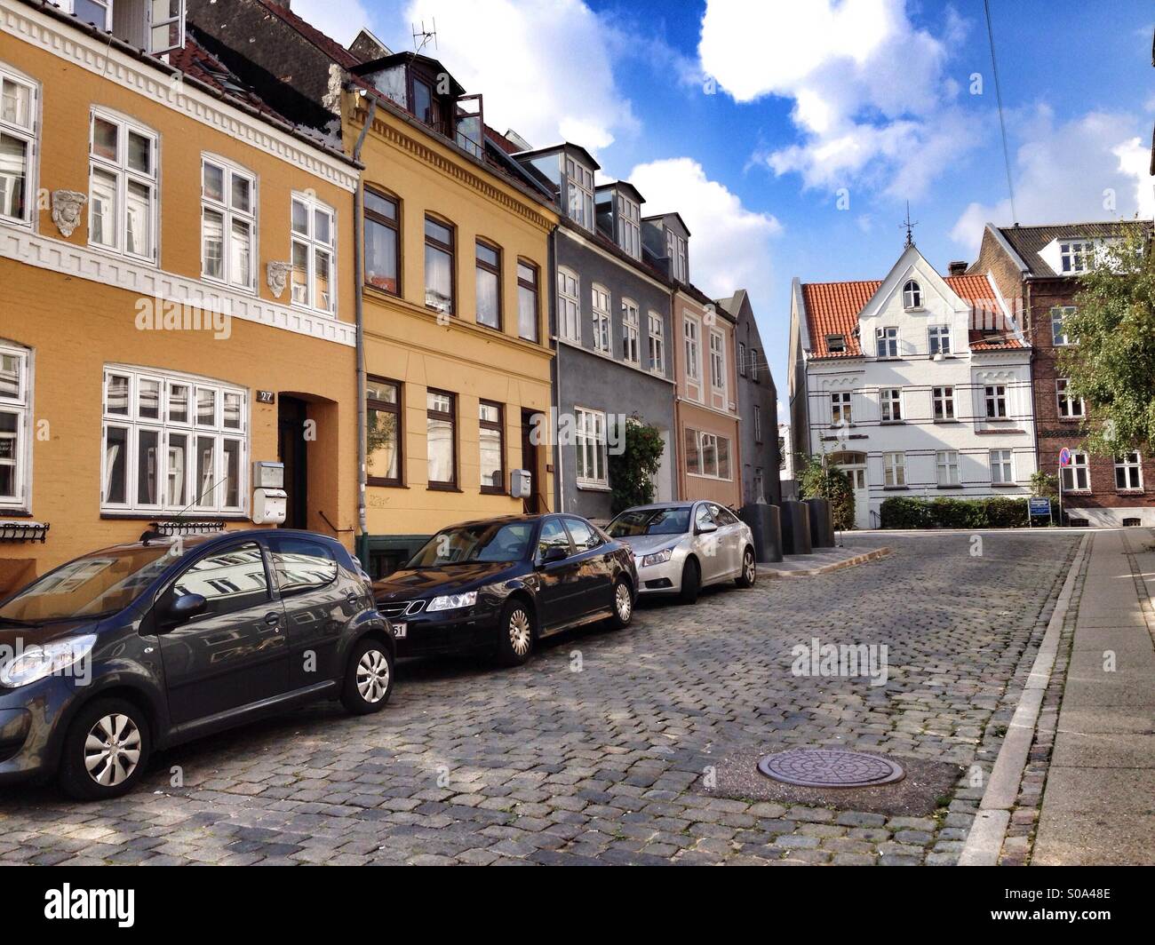 Scandinavian city scene, colored houses in a narrow stone street in a sunny day, with a blue sky with a few clouds, in the center of Aarhus, Jutland peninsula, Denmark Stock Photo