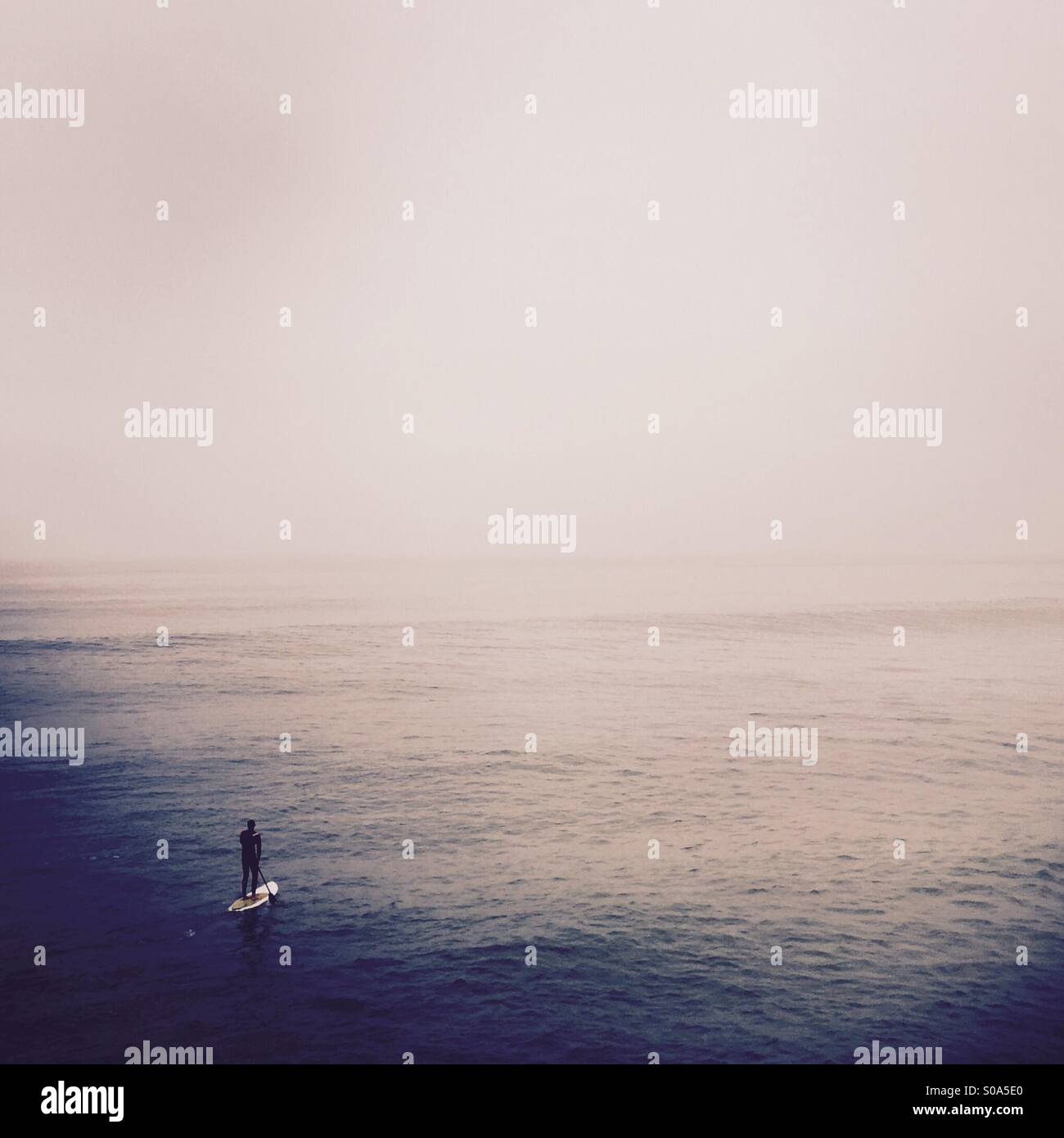 Sand up surfer paddles out on a foggy day. Manhattan beach, California USA. - Smartphone Captured Stock Image