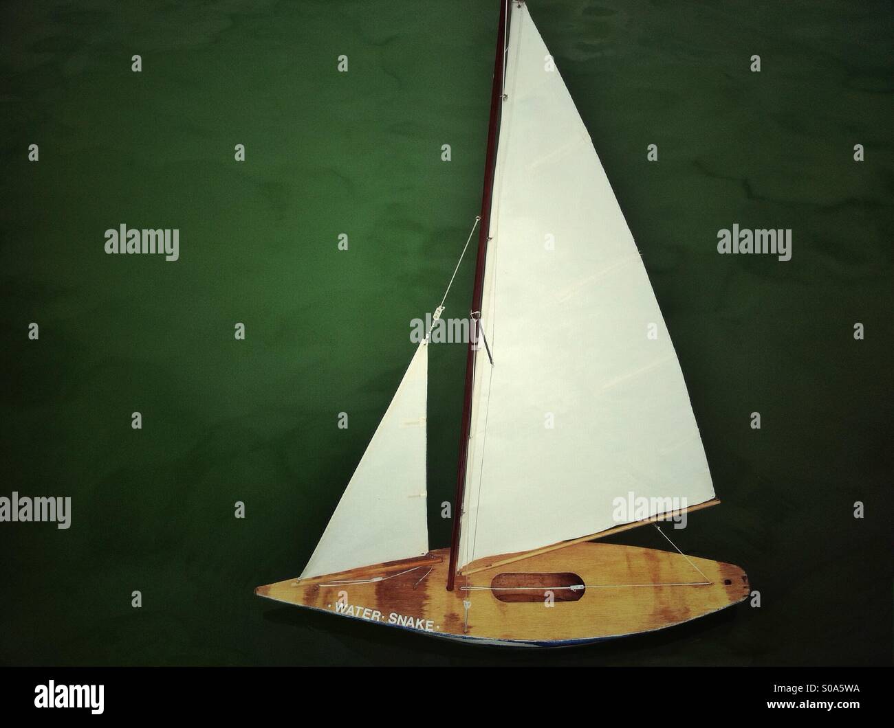 Small wooden sailboat model on green water - Smartphone Captured Stock Image