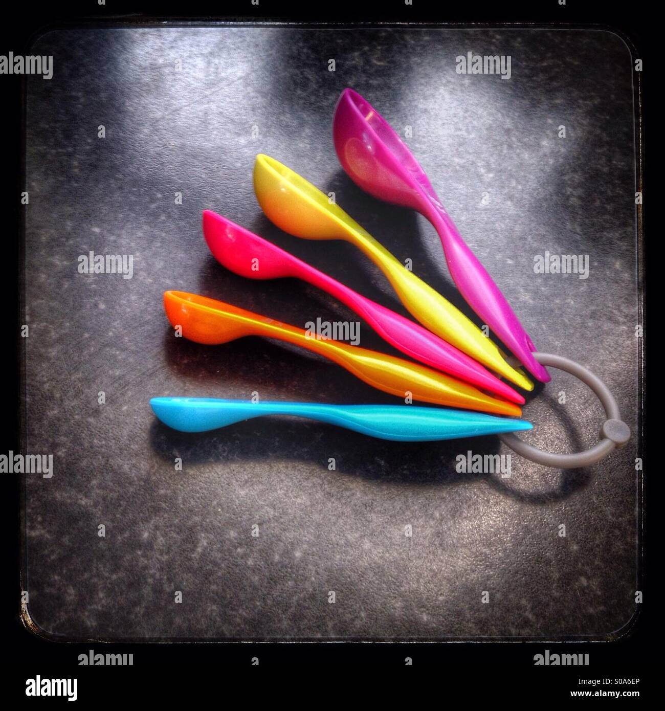 A set of five colourful measuring spoons on a black marbled worktop - Smartphone Captured Stock Image