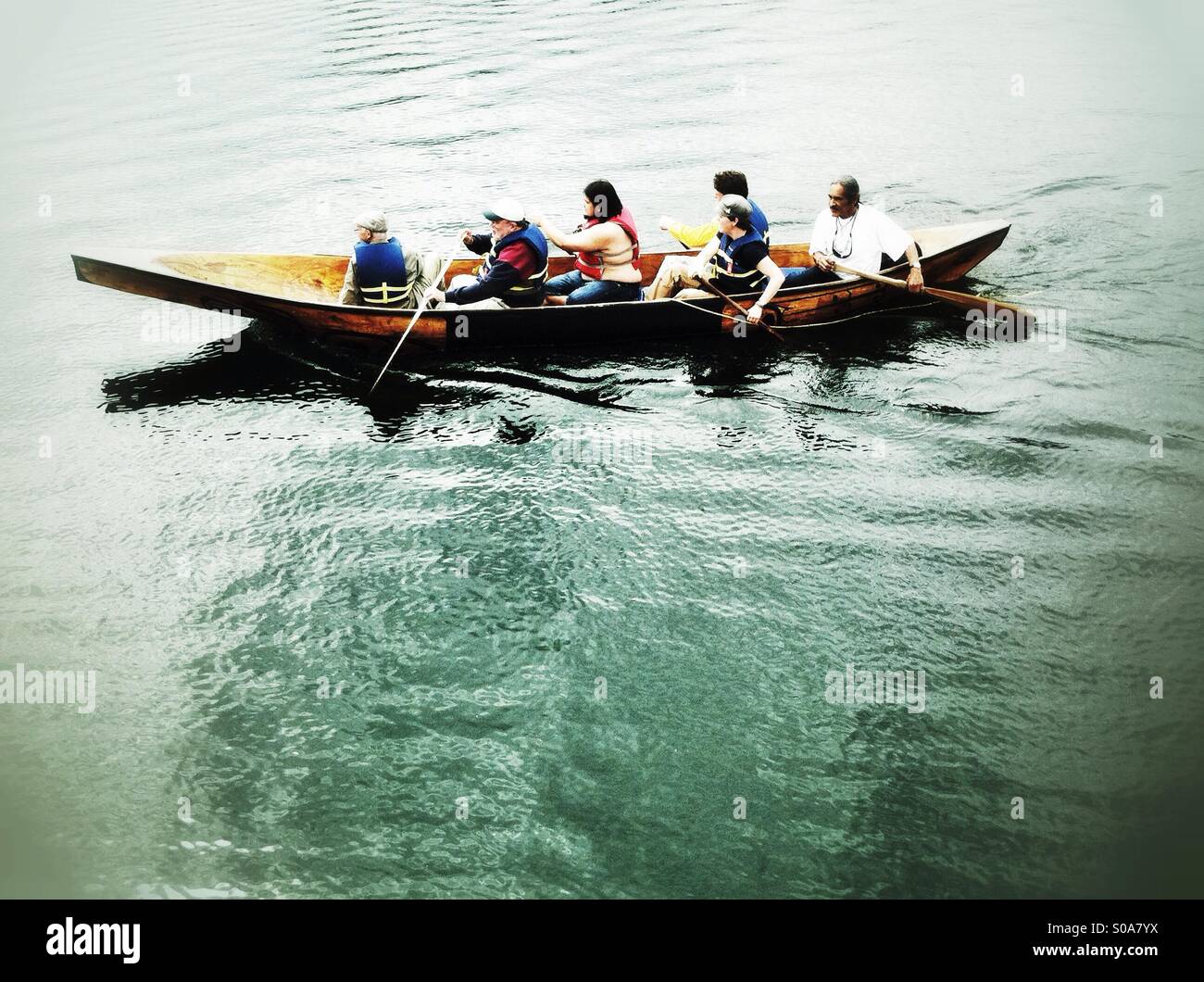 Six people paddle traditional Native American canoe carved out of a cedar tree - Smartphone Captured Stock Image