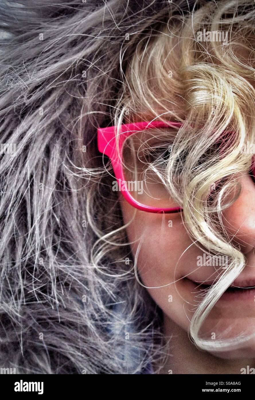 Young girl wearing furry hood and red glasses with face obscured by curly blond hair Stock Photo