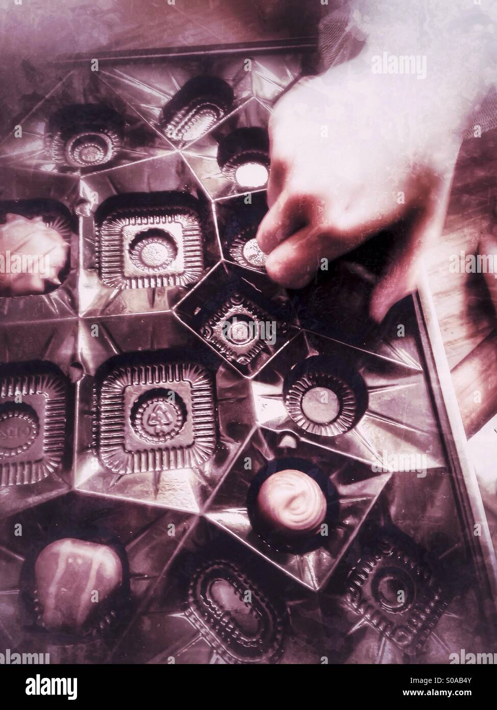 A child picking up candy from a box of chocolates. - Smartphone Captured Stock Image