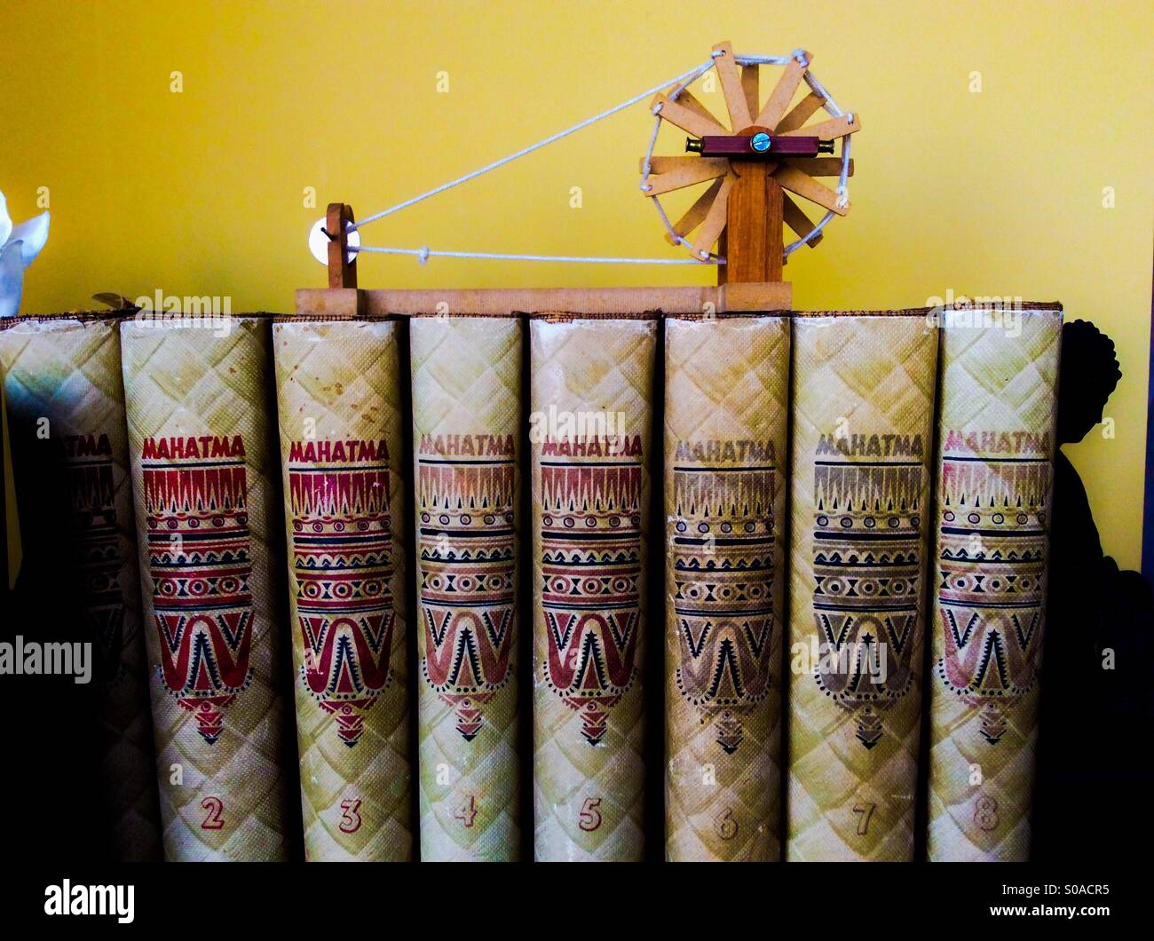 The Complete Mahatma Gandhi. A dedicated souvenir. Several volumes of his writings, bookended by Buddha, a model of his spinning wheel - charkha - on top, in a Canadian home. - Smartphone Captured Stock Image