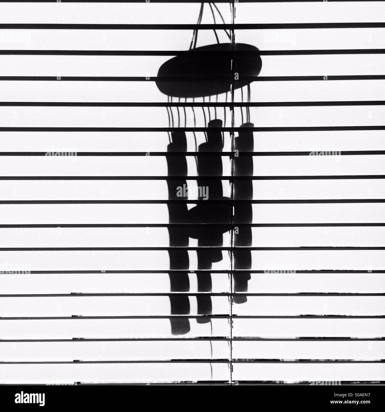 Silhouette of wind chime behind Venetian blind Stock Photo