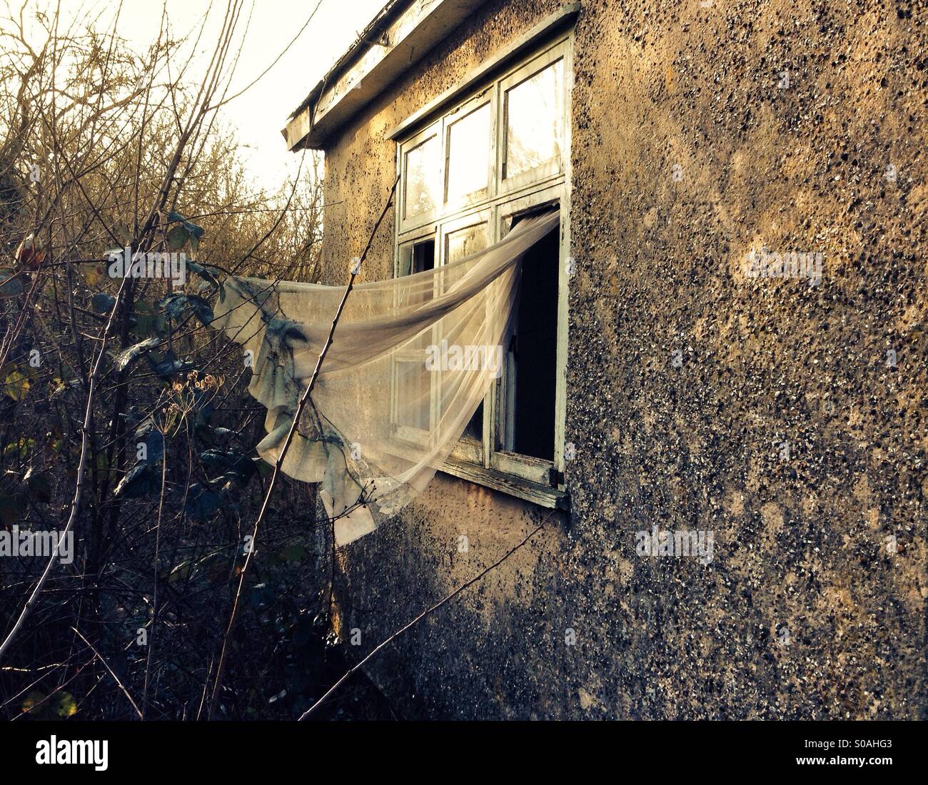 Abandoned home with broken windows and curtains blowing in the wind - Smartphone Captured Stock Image