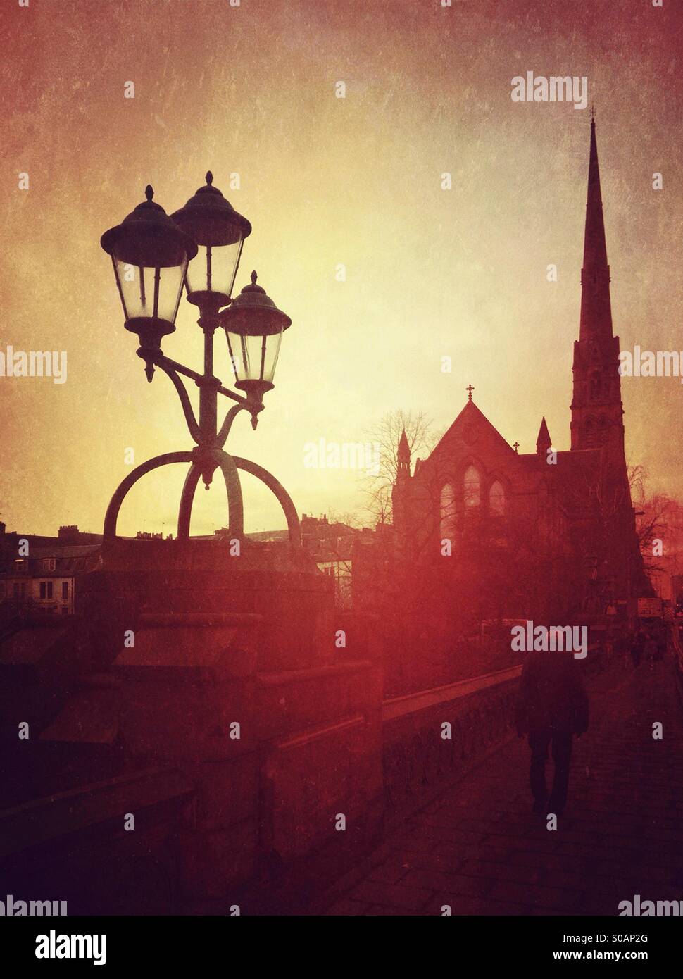 Man walking on bridge between Victorian lamppost and church. - Smartphone Captured Stock Image