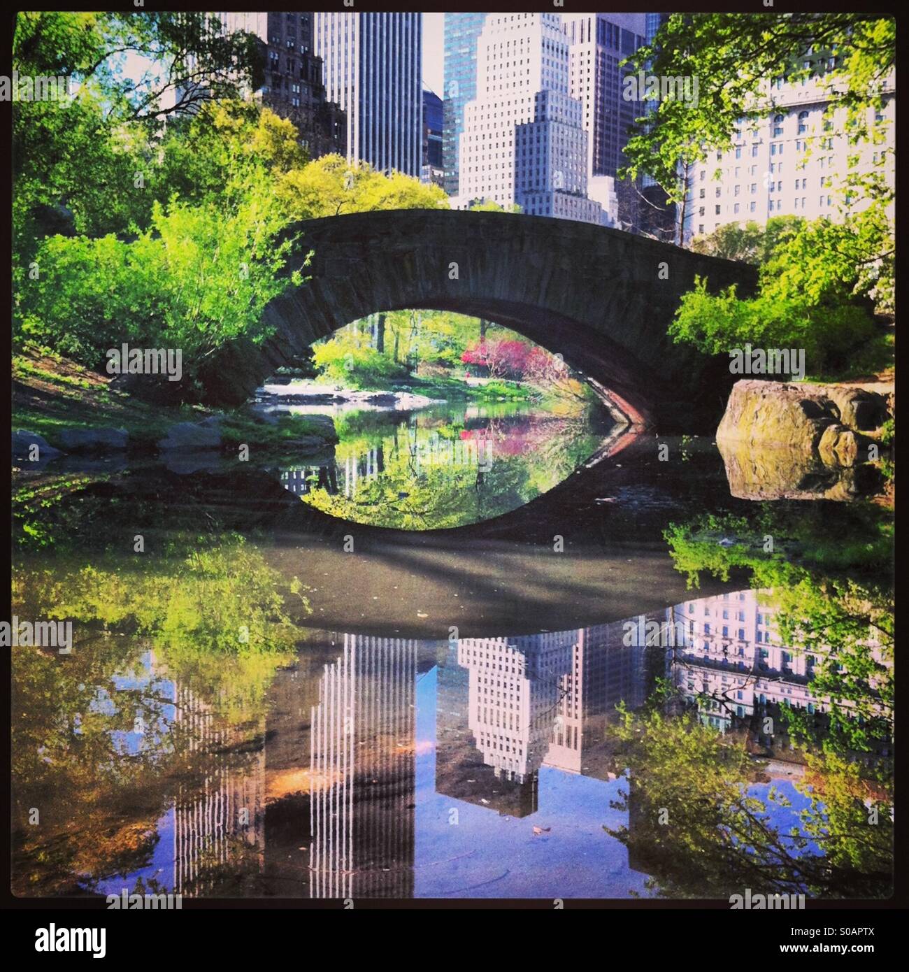 View of Gapstow Bridge in Central Park with buildings reflected in pond. Stock Photo