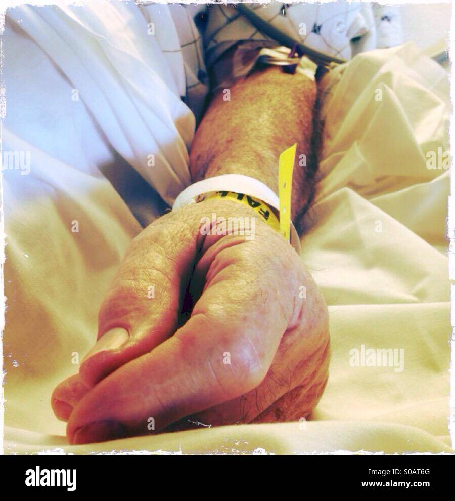 An elderly, male patient's arm with an iv.  A yellow bracelet with the word fall on it is on his wrist. - Smartphone Captured Stock Image