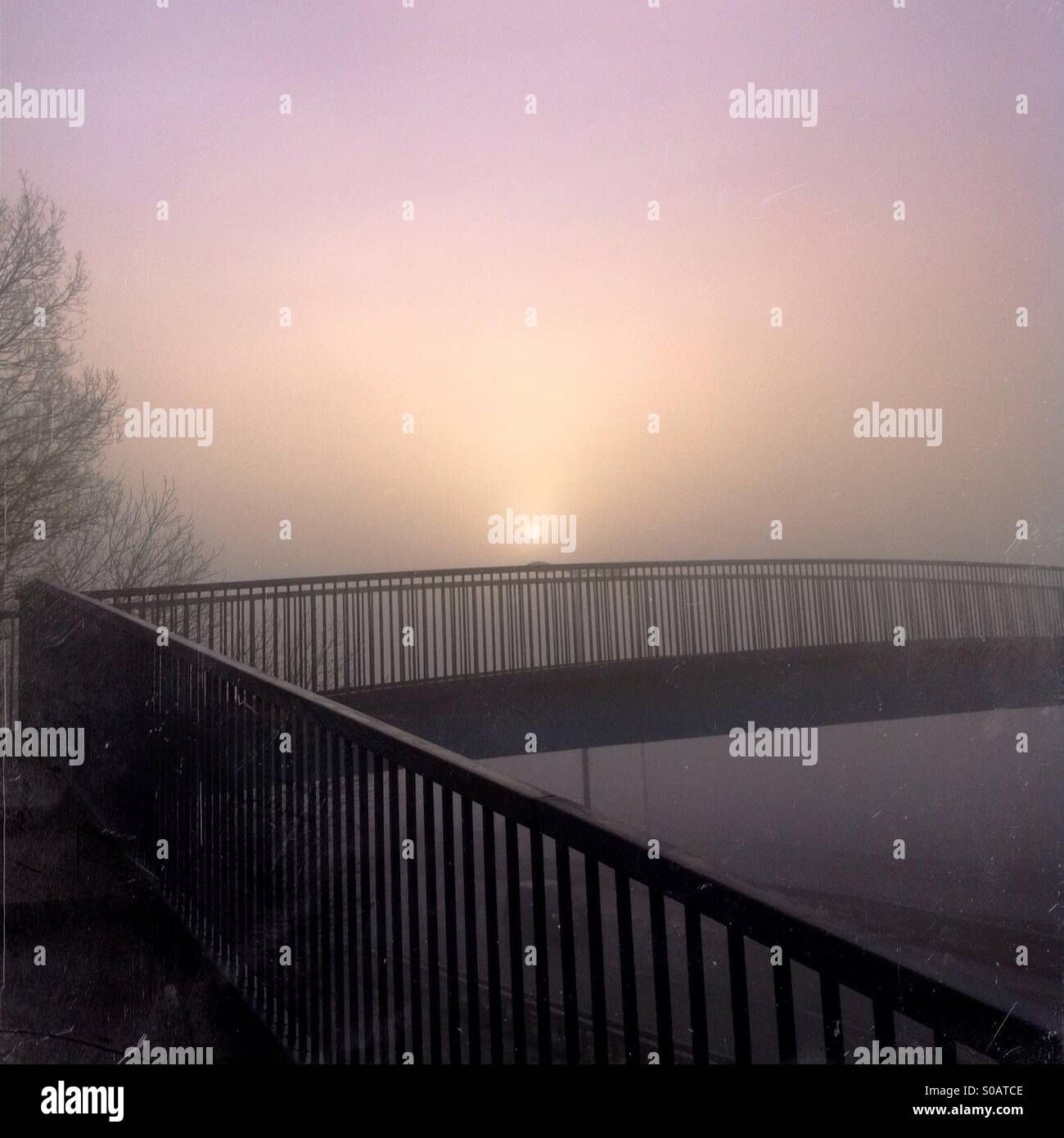 Footbridge and rising sun in fog. Stock Photo