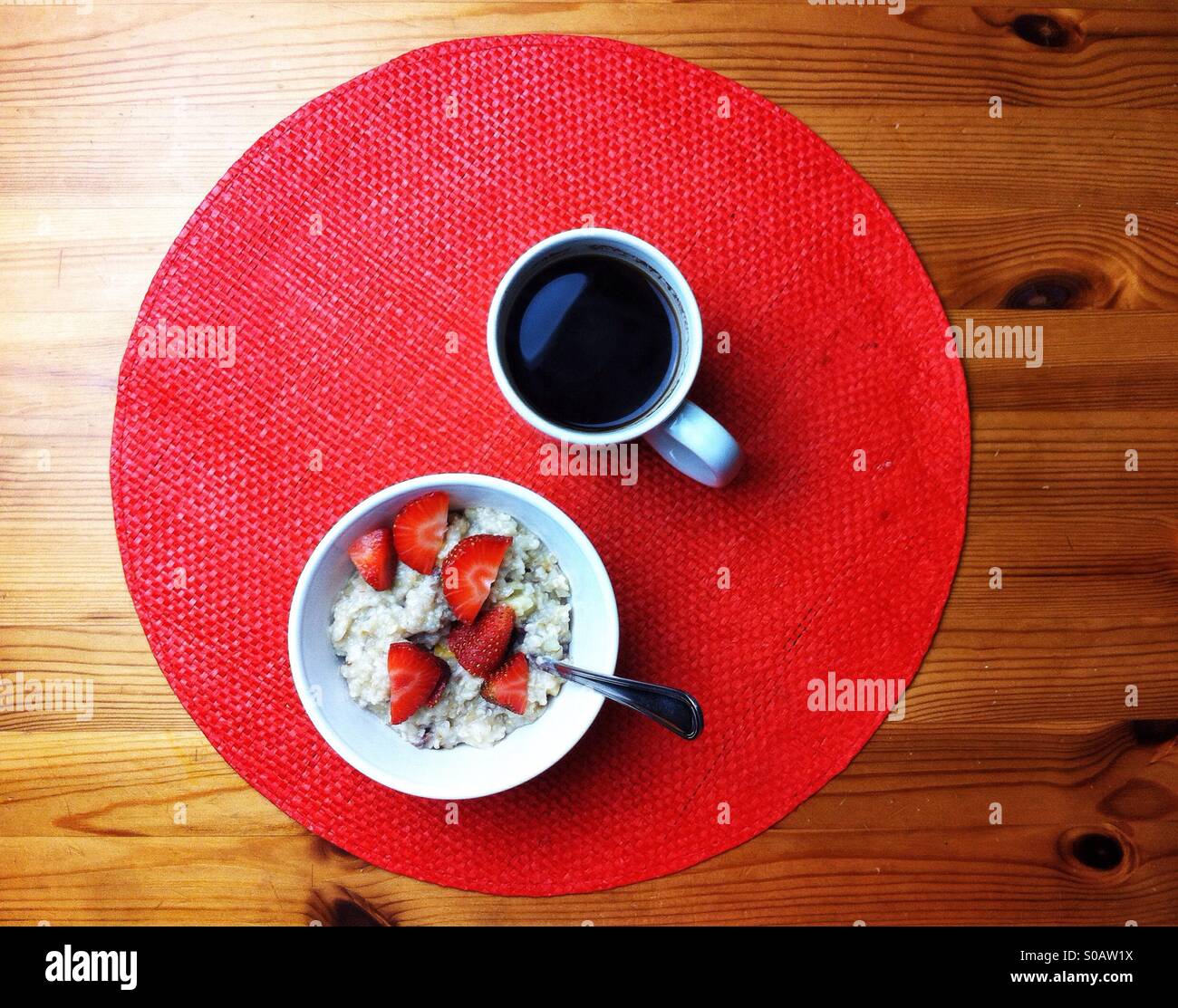 Simple breakfast on red place mat and pine wooden table wit oatmeal and black coffee - Smartphone Captured Stock Image