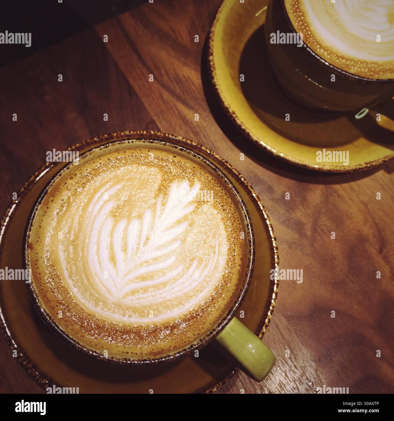 Two flat white coffee drinks on a wooden table - Smartphone Captured Stock Image