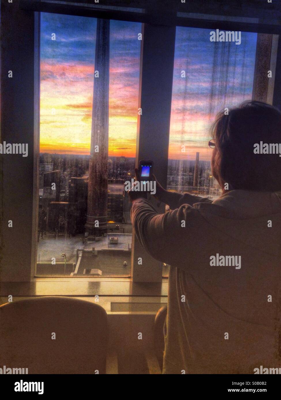 A woman taking a photo of a sunset with an iPhone. - Smartphone Captured Stock Image