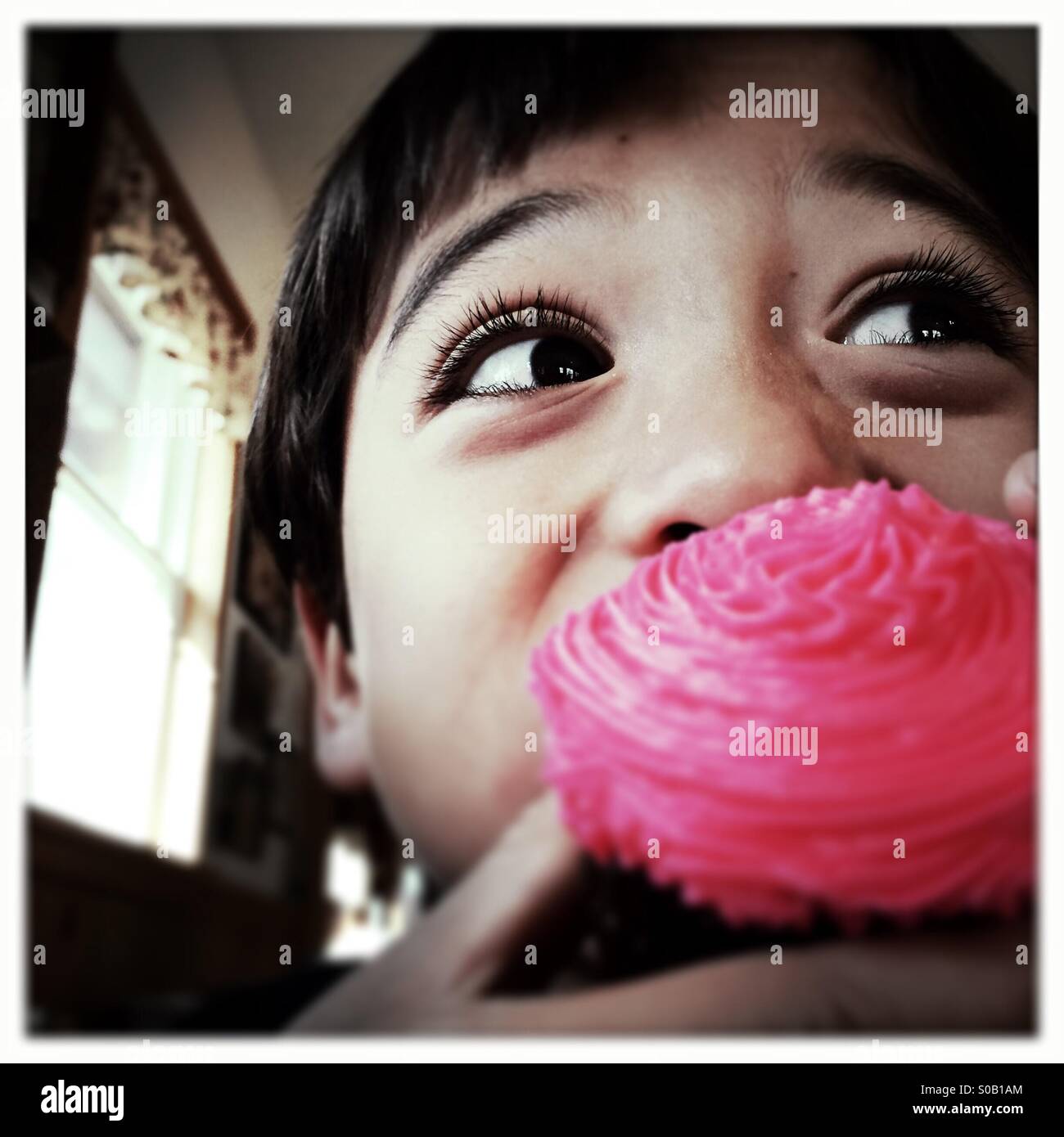 A six year old Asian Caucasian mixed race boy takes a bite of a cupcake. - Smartphone Captured Stock Image