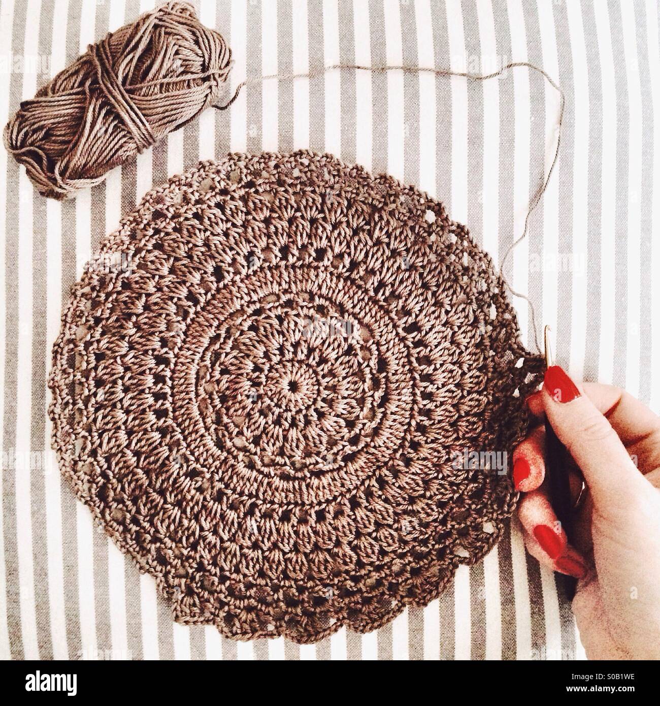Light brown crochet doily with yarn, and hand holding crochet hook