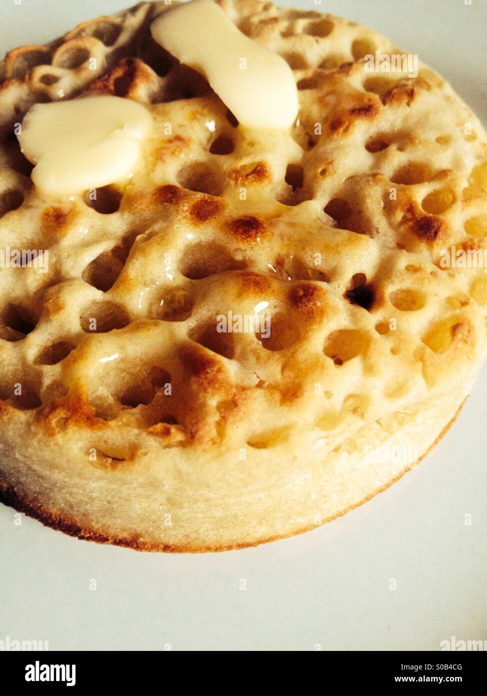 Hot buttered crumpet on a white plate Stock Photo