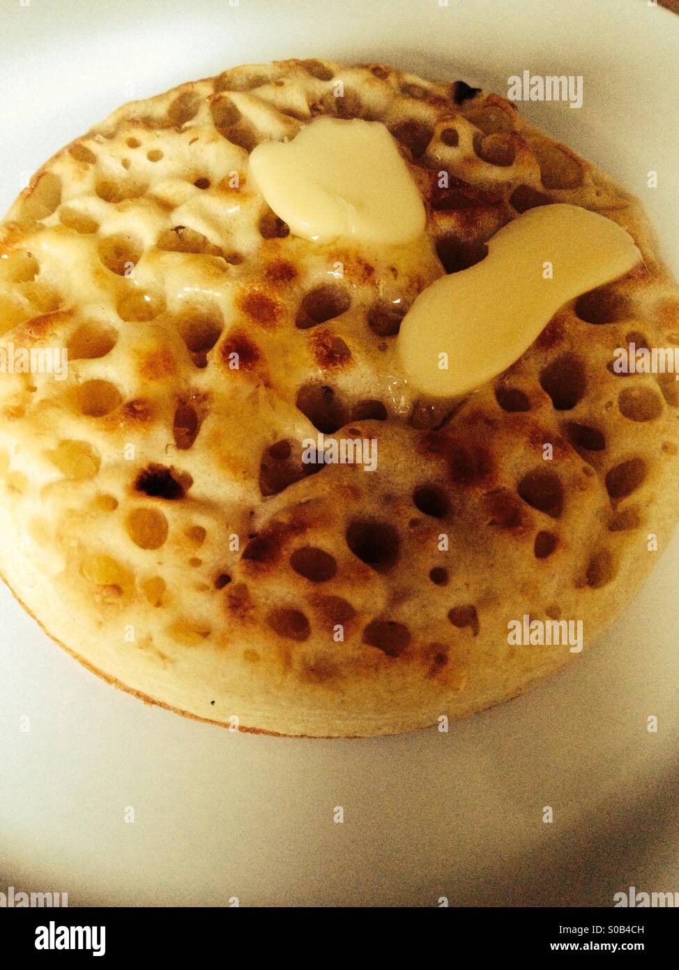 Hot buttered crumpet on a white plate Stock Photo