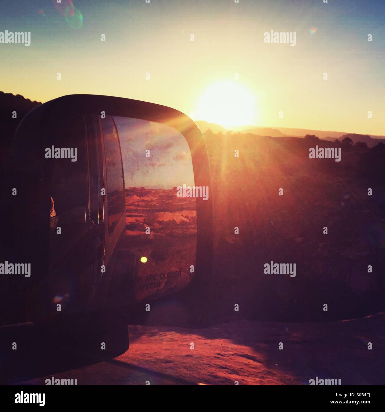 The sunset over Fins -n-Things off-road trail in Moab, UT reflects in a Jerp's rearview mirror. Stock Photo