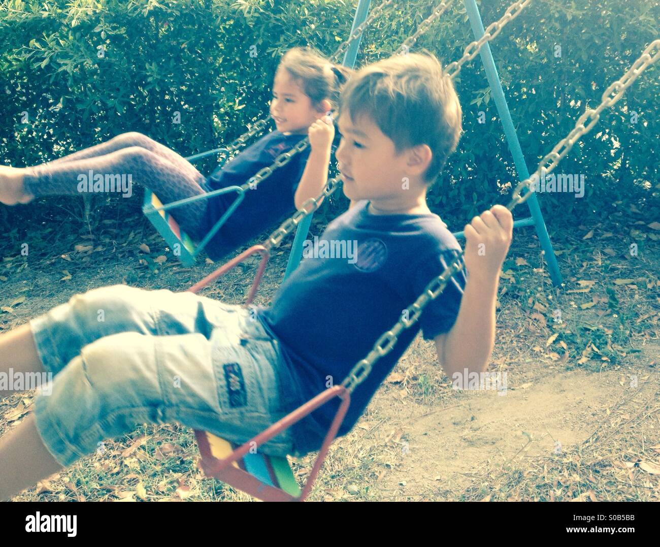 Two 5 year-old children playing on swings in a playground. Stock Photo