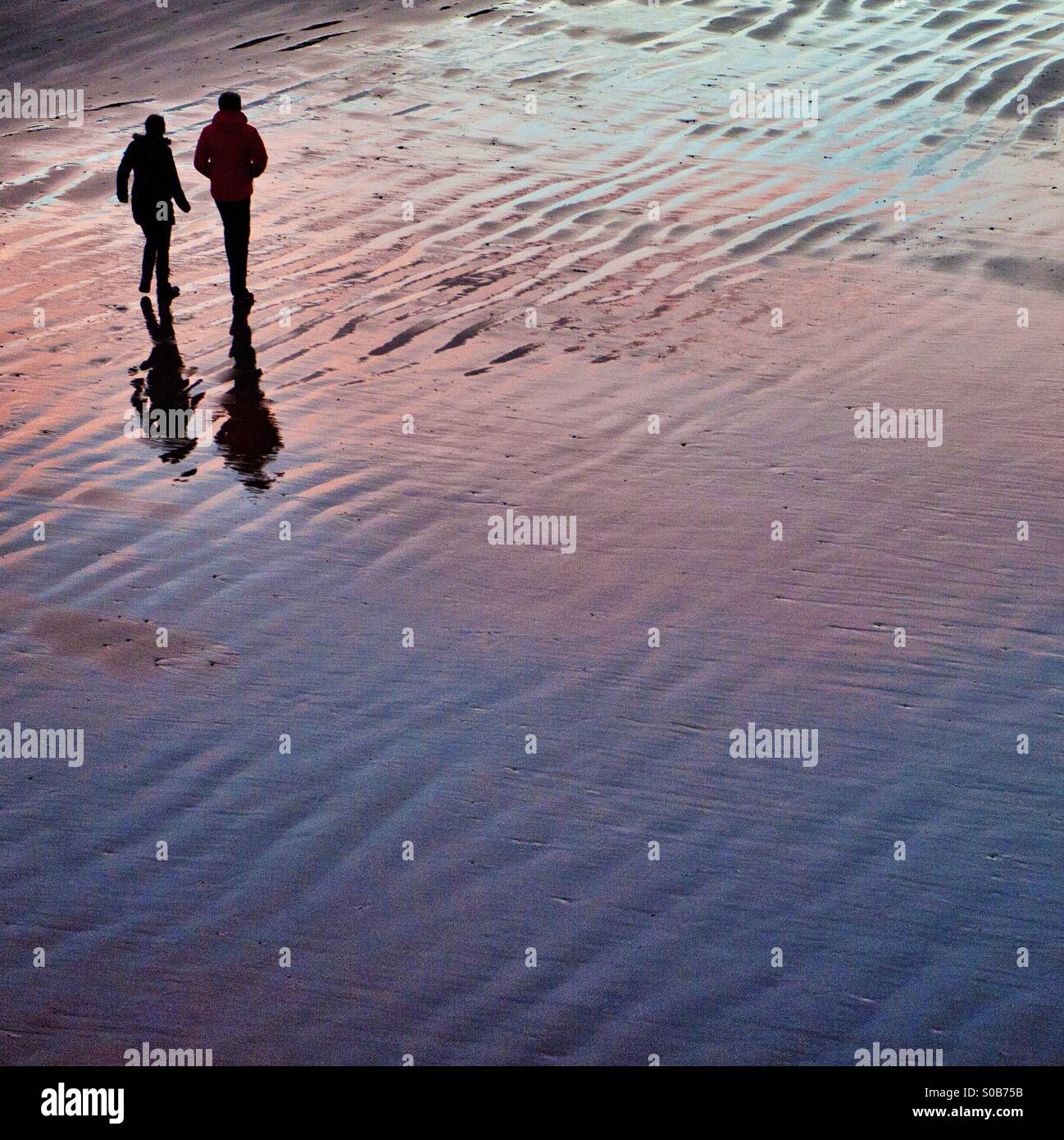A couple walk along Saltburn beach with the sunset reflecting in the water. Stock Photo