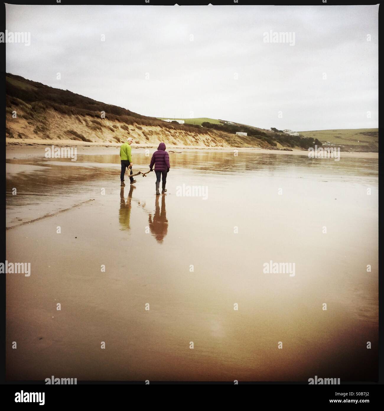 Couple walking across beach in winter carrying driftwood - Smartphone Captured Stock Image