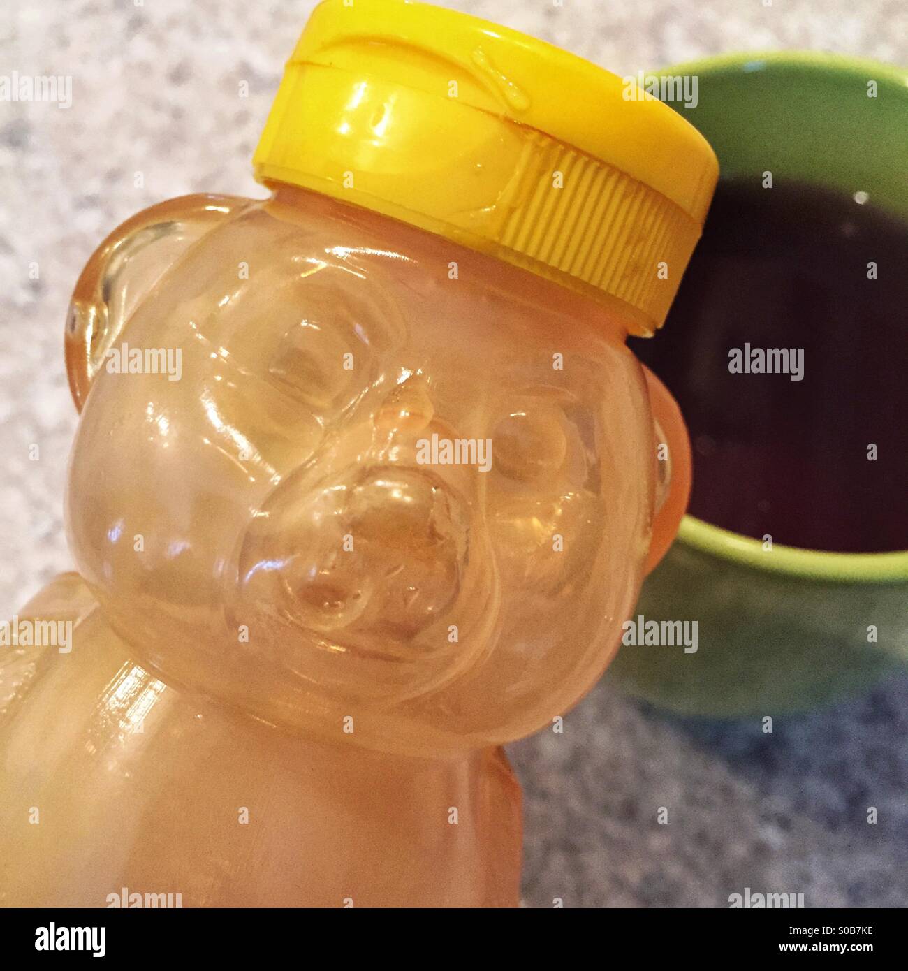 Honey bear bottle of liquid honey alongside a cup of herbal tea. Stock Photo