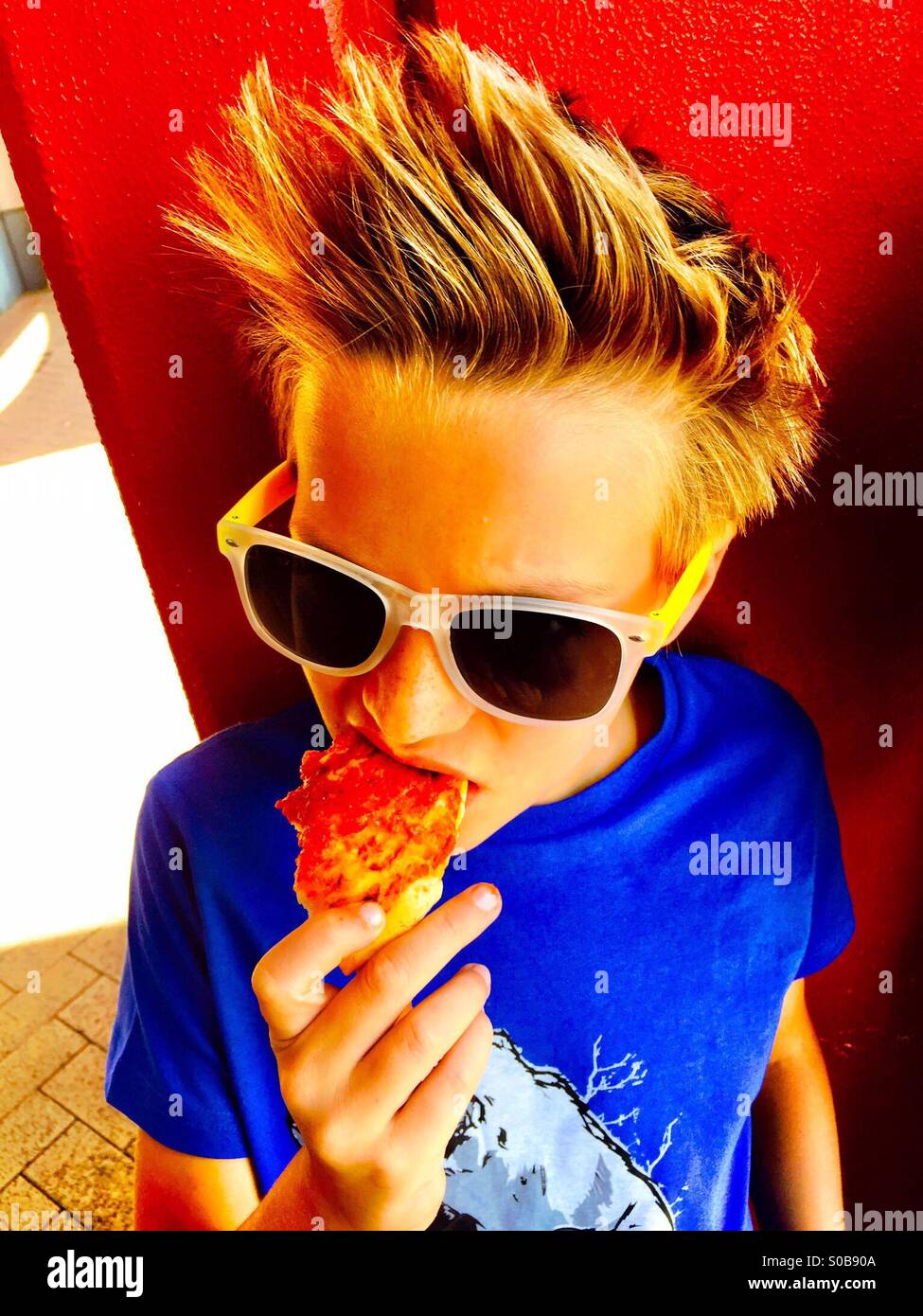 A colourful photo of a boy eating pizza Stock Photo