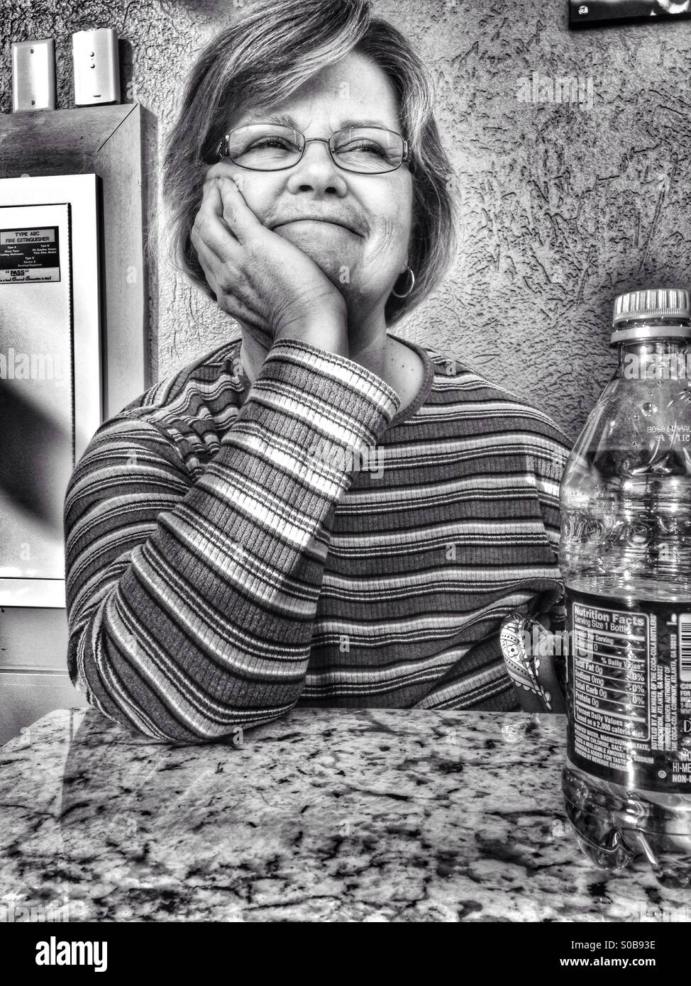 A smile from a tired lady sitting at a table (b/w). - Smartphone Captured Stock Image