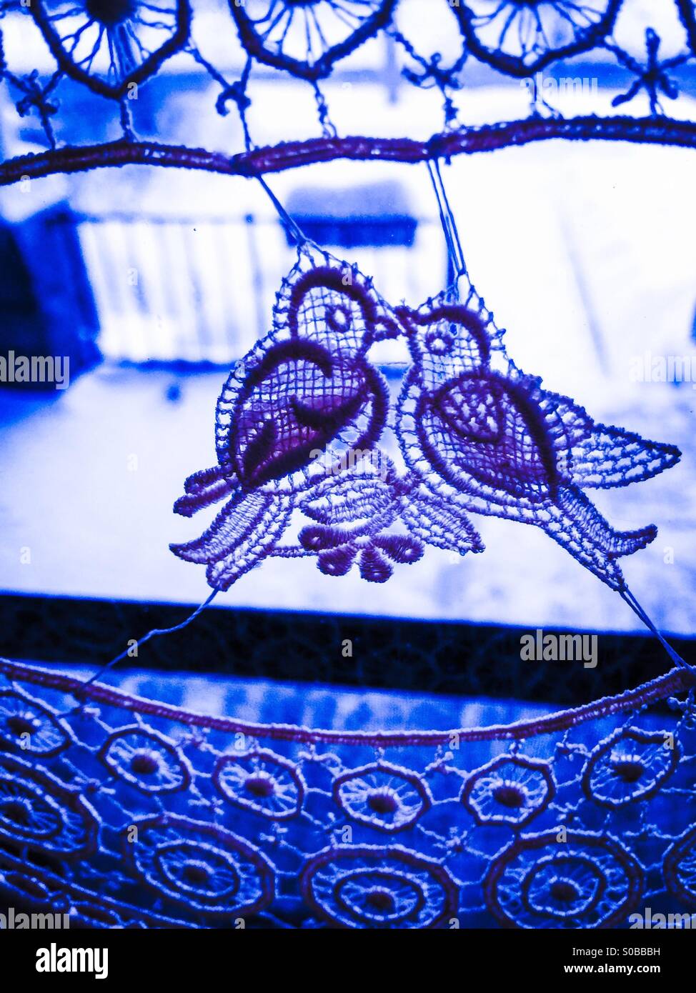 Blue lovebirds. An icon of love, mating, companionship, partnership, association, in many cultures. Not just an item of decor. Delicate lace. Threads of love. Suspended. - Smartphone Captured Stock Image