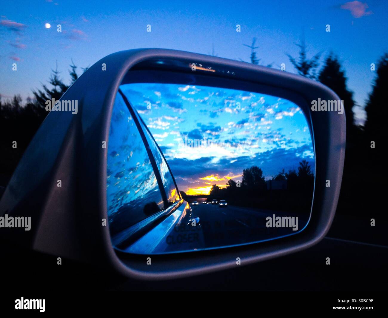 Reflection of traffic, clouds and sunset in the side mirror of car. - Smartphone Captured Stock Image
