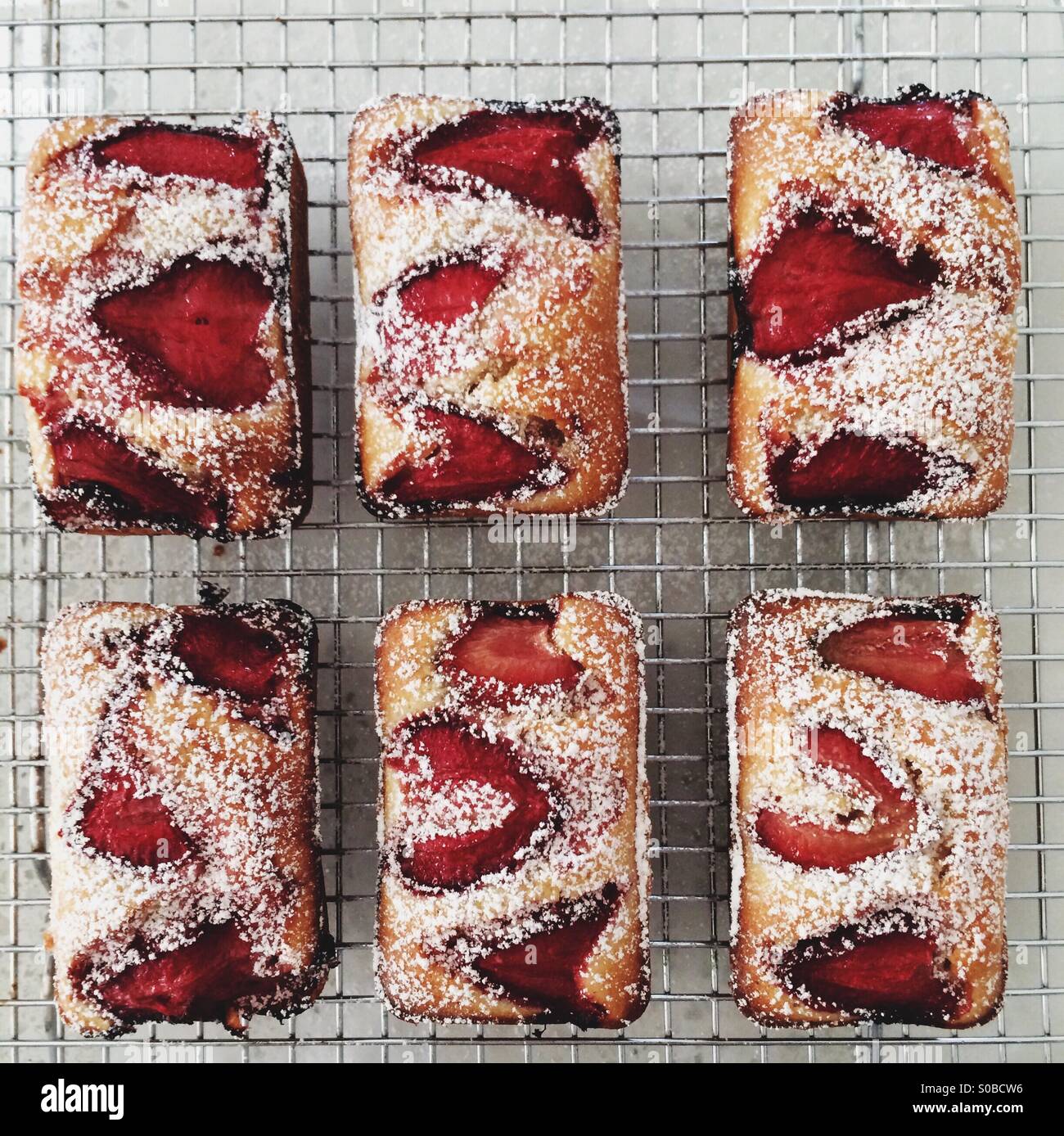 Small strawberry cakes cooling on wire rack, light background Stock