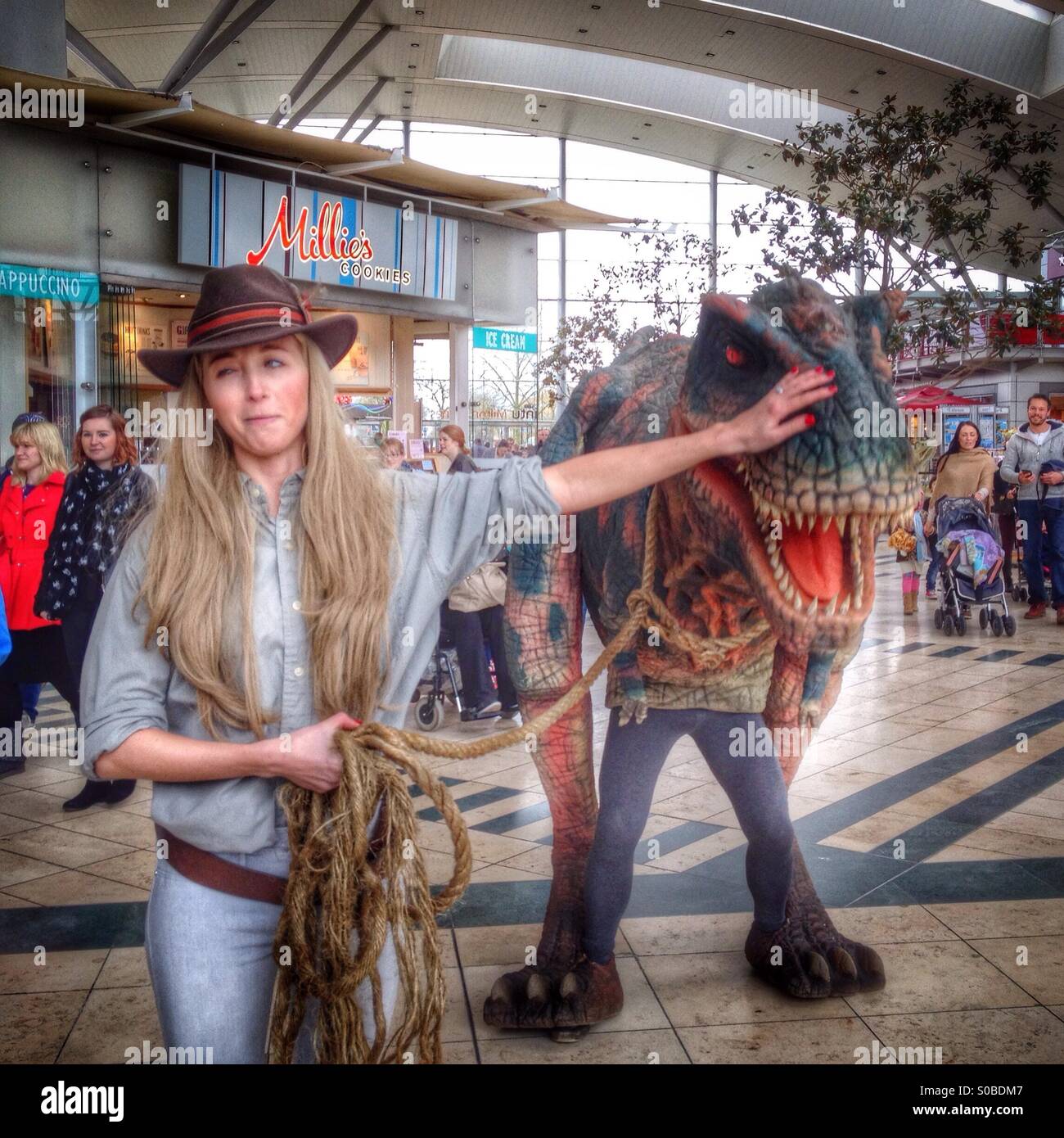Girl in a park ranger outfit takes a man in a Dinosaur for a walk; Milton Keynes shopping centre. - Smartphone Captured Stock Image