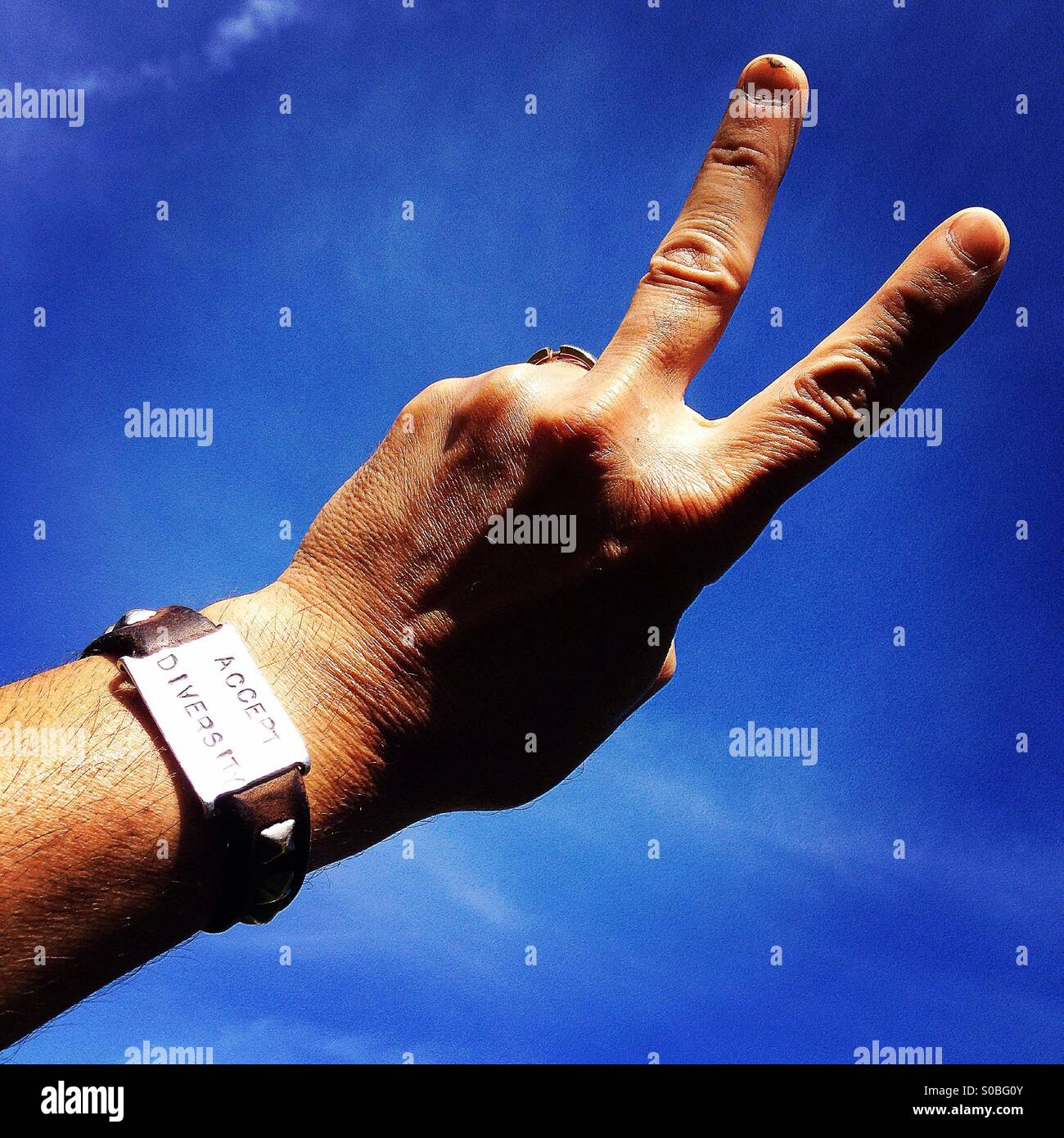 'Accept Diversity' leather and steel bracelet on man making two finger peace sign at sky Stock Photo