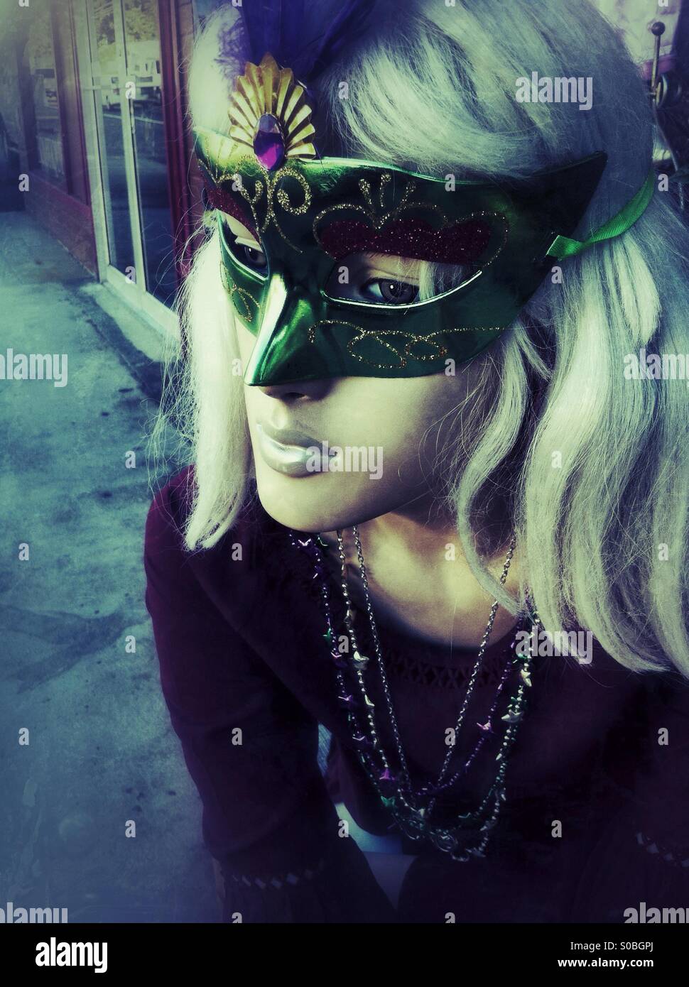 blond female manikin on a street wearing a Venetian mask with peacock feathers - Smartphone Captured Stock Image