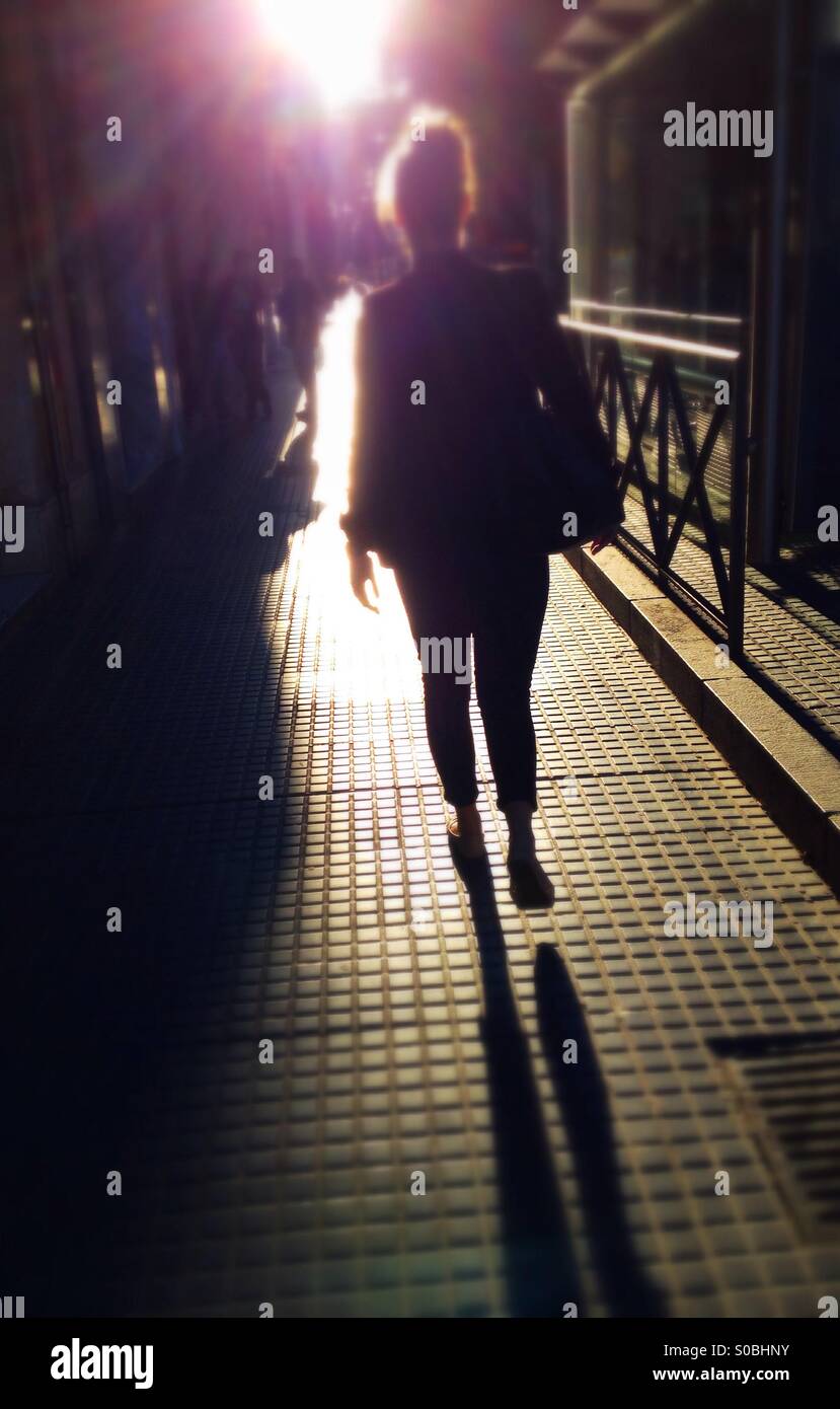Back view of woman walking along street into the sun - Smartphone Captured Stock Image