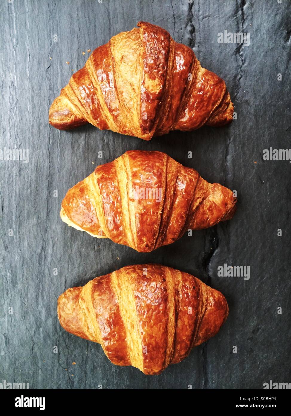Three croissants from Balthazar Bakery in Englewood, NJ, USA seen from above on a slate slab. - Smartphone Captured Stock Image